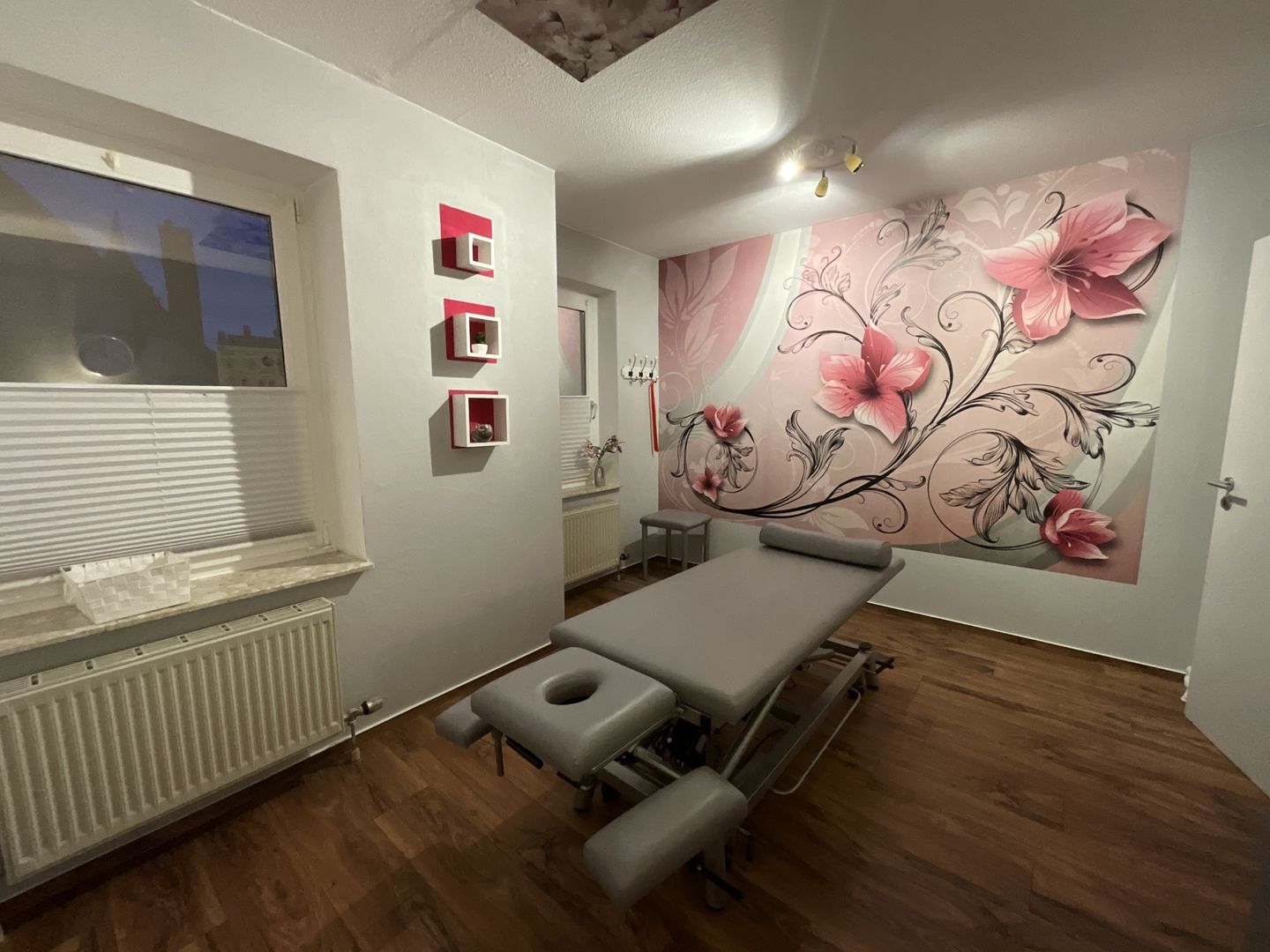 Therapieraum mit einem Massagetisch und einer Wand, die mit Blumen dekoriert ist.
